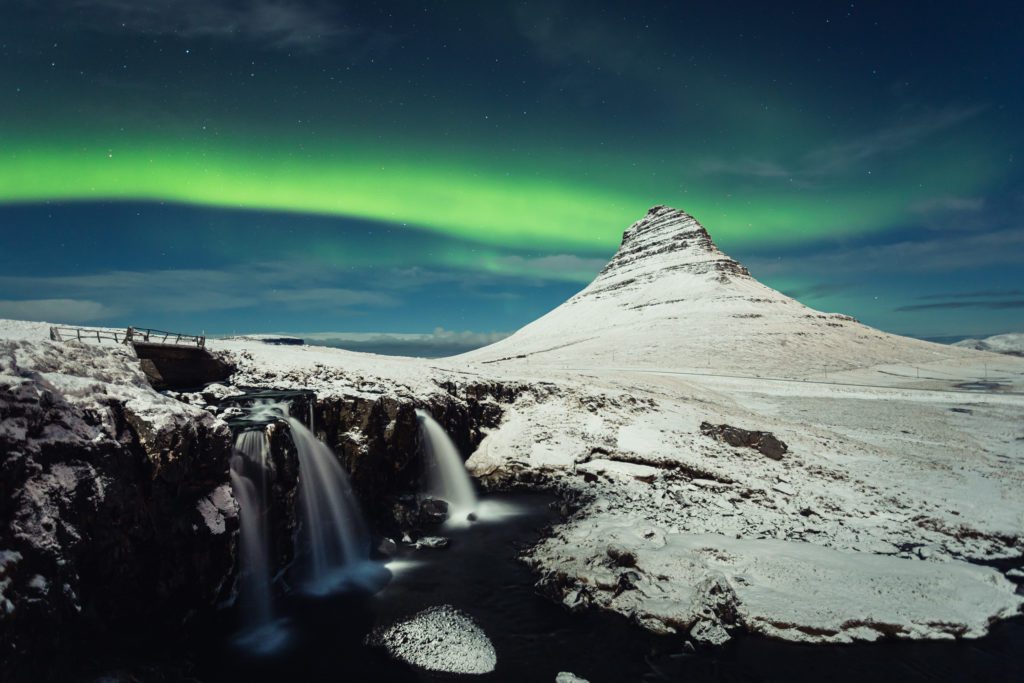 Aurora dancing above Kirkjufell mountain with Kirkjufellsfoss waterfall in the foreground, Snæfellsnes.