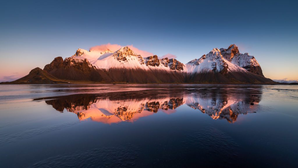Pink sunset alpenglow on Vestrahorn mountains reflected in still water at Stokksnes.