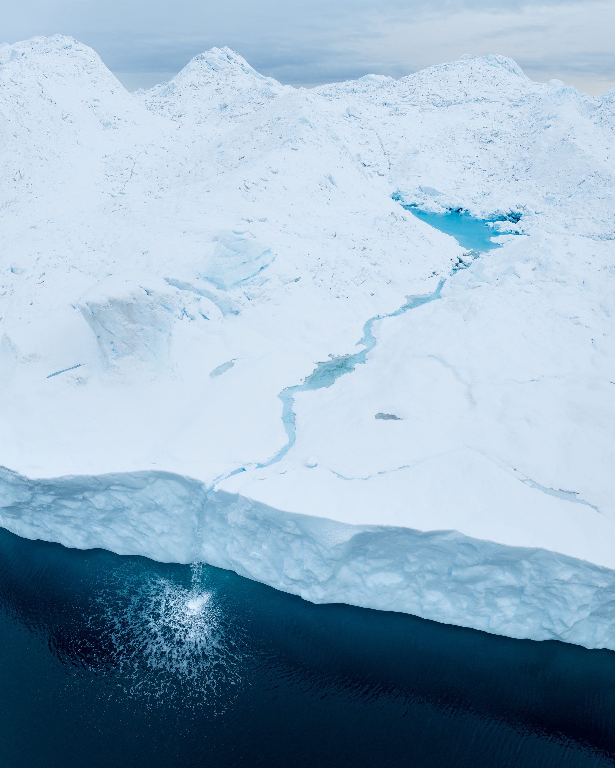 A drone shot of a small waterfall pouring down an iceberg