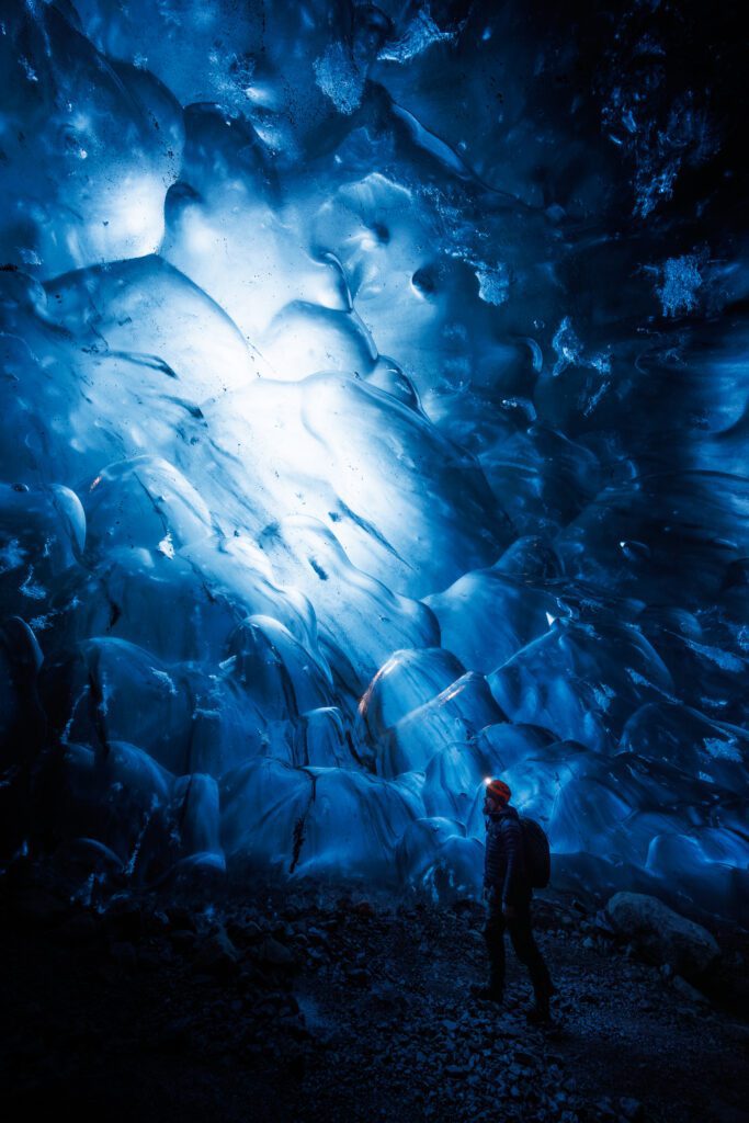 Person with a headlamp looking up at the glowing blue ceiling of a Vatnajökull ice cave.