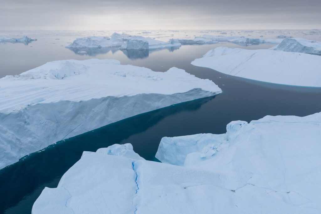 Aerial drone view of cloud-shrouded snowy peaks above a Greenland fjord.