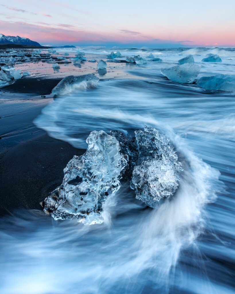 Iceberg stranded on black sand at sunrise on Fellsfjara, Iceland's Diamond Beach.