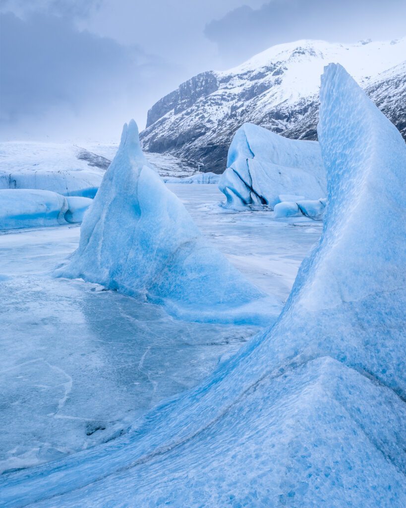 Sculpted blue glacier ice rising from a frozen plain at the foot of Skaftafellsjökull glacier in Iceland.