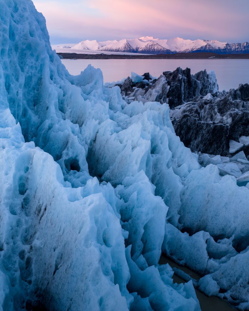 Massive blue ice spires at Fjallsárlón glacier lagoon at twilight with snowy peaks behind, Iceland.