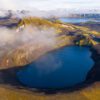Aerial drone view of Bláhylur crater lake, ringed by golden moss and rust-red scoria slopes in Fjallabak, Iceland.
