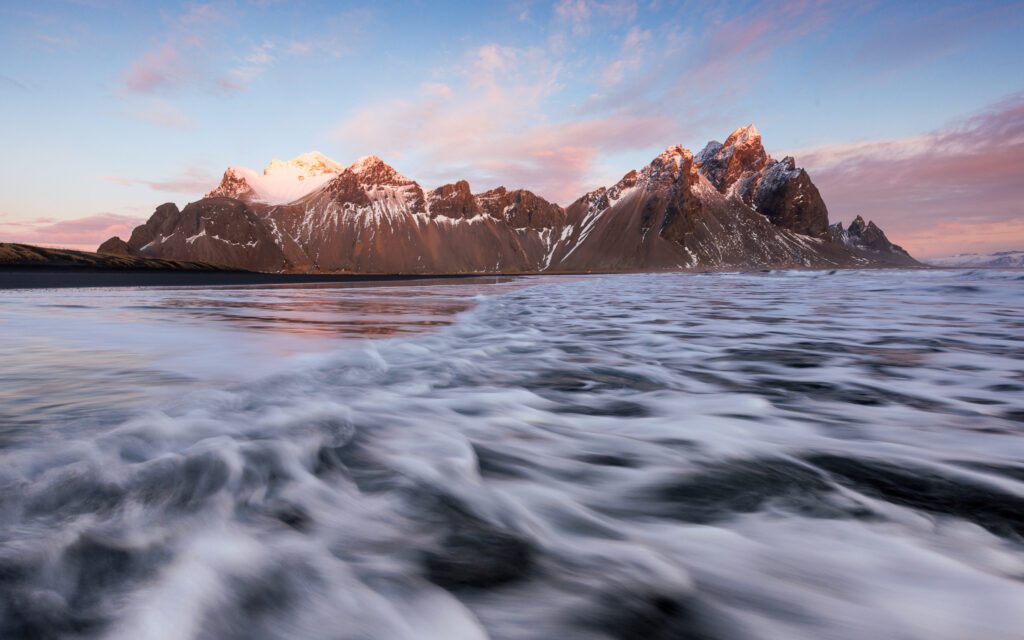 Pink clouds above snow-capped Vestrahorn while surf races across the black sand at Stokksnes.